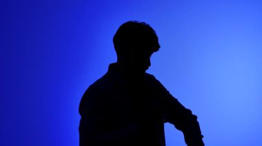 Profesyonel bir stüdyonun sahne arkasında, bir erkek fotoğrafçı kamerasının lensini değiştiriyor ve yaratıcı neon mavi ışıklandırmalı bir stüdyoda fotoğraf çekiyor..