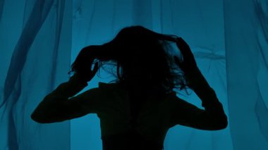 Dalgalı saçlı bir kadının sanatsal silueti mavi arka planı olan şeffaf bir plastik çarşaf karşısında gizemli bir şey çağrıştırıyor..