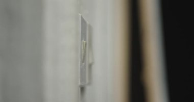 Bir insan eli odadaki beyaz duvarın düğmesini çeviriyor. Işık söner, oda karanlığa gömülür..