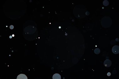 Karanlık bir arka planda yumuşak bulanık bokeh çemberleri rüya gibi ve soyut bir görsel etki yaratır. Siyah bir zemin üzerinde beyaz toz, toz veya kar parçacıkları izole. Üst üste efektli arkaplan.