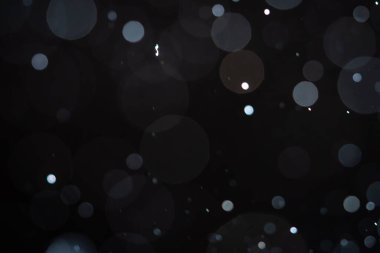 Karanlık bir arka planda yumuşak bulanık bokeh çemberleri rüya gibi ve soyut bir görsel etki yaratır. Siyah bir zemin üzerinde beyaz toz, toz veya kar parçacıkları izole. Üst üste efektli arkaplan.