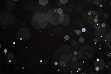Karanlık bir arka planda yumuşak bulanık bokeh çemberleri rüya gibi ve soyut bir görsel etki yaratır. Siyah bir zemin üzerinde beyaz toz, toz veya kar parçacıkları izole. Üst üste efektli arkaplan.