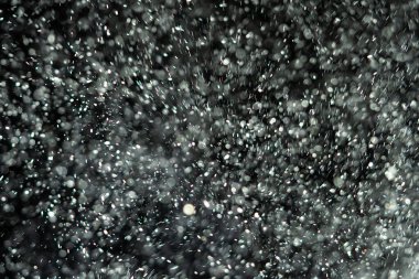 Küçük toz parçacıkları dumanlı havada rastgele uçuyor, reklam nesneleri için boş bir şablon. Beyaz toz parçacıkları loş ışıkta boş siyah zıt bir zıt arkaplan karşısında.