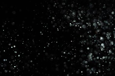 Küçük toz parçacıkları dumanlı havada rastgele uçuyor, reklam nesneleri için boş bir şablon. Beyaz toz parçacıkları loş ışıkta boş siyah zıt bir zıt arkaplan karşısında.