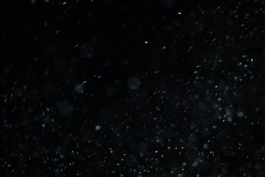 Siyah bir arka plan üzerinde Bir ışık ışını içinde yüzen toz yükselen küçük parçalar. Uzayda hızla hareket eden rüzgar tarafından uçurulmuş gibi rastgele dönüyor. Her biri bağımsız ve dinamik uçan.