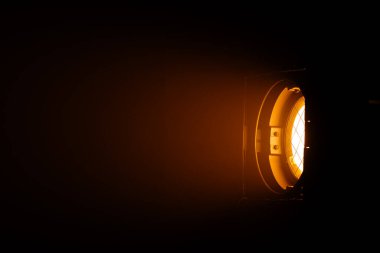 Karanlık bir odayı aydınlatan güçlü bir turuncu spot ışığını kapat ve dramatik bir ışık efekti yarat. Sahne arkasında ışıklandırma ekipmanları.