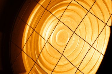 Parlayan turuncu sahne ışıkları, metal parçaları, cıvataları ve koruyucu tel örgüleri gösteriyor. Sahne arkasında ışıklandırma ekipmanları.