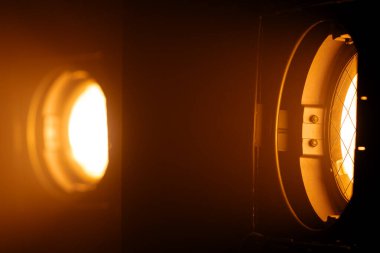 İki güçlü stüdyo ışıkları karanlıkta sıcak turuncu ışıklar yayarak çarpıcı bir sinematik ışık efekti yaratır. Sahne arkasında ışıklandırma ekipmanları.