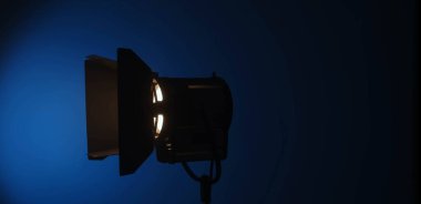 Sinematik ışıklandırma kullanılarak, arka planda mavi bir gradyan ile sıcak bir turuncu stüdyo spot ışığı açılır. Sahne arkasında ışıklandırma ekipmanları.