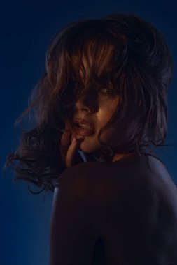 Genç bir kadın modelin büyüleyici bir portresi, dramatik bir mavi ışıkla aydınlatılmış gizemli ve cezbedici bir atmosfer yaratıyor..