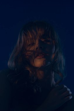 Genç bir kadın modelin büyüleyici bir portresi, dramatik bir mavi ışıkla aydınlatılmış gizemli ve cezbedici bir atmosfer yaratıyor..