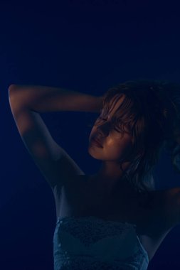 Genç bir kadın modelin büyüleyici bir portresi, dramatik bir mavi ışıkla aydınlatılmış gizemli ve cezbedici bir atmosfer yaratıyor..