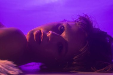 Yumuşak mor ışıkla aydınlanan, sakin ve sanatsal bir kadın portresi, sakin bir atmosfer yaratıyor..