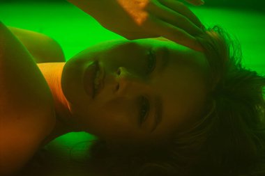 Yumuşak yeşil ışıkla aydınlatılmış, sakin ve sanatsal bir kadın portresi, sakin bir atmosfer yaratıyor..