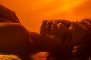 Bir kadının sakin ve sanatsal portresi uzanmış, yumuşak sarı ışıkla aydınlatılmış, sakin bir atmosfer yaratıyor..