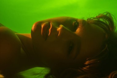 Yumuşak yeşil ışıkla aydınlatılmış, sakin ve sanatsal bir kadın portresi, sakin bir atmosfer yaratıyor..