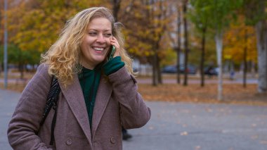 Sonbahar boyunca şehir parkında ceketli bir kadın kulağına telefon dayamış ve endişeli görünüyor..