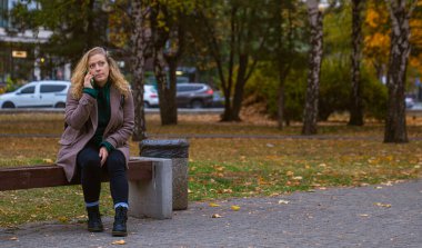 Sonbaharda bir şehir parkında kürklü bir kadın akıllı telefonuyla konuşuyor. Sonbahar parkında huzurlu bir sonbahar havası..