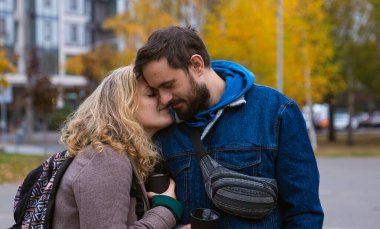 Bir çift, sonbaharda renkli yeşillikler ve binalarla çevrili bir şehir parkında hassas bir anı paylaşıyor..