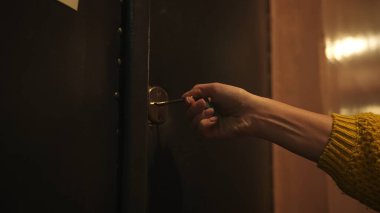 Kapının kilidini açıp anahtarı çeviren bir elin kapatılması, sıcak ışıkla aydınlatılması, güvenlik ve ev erişiminin göstergesi.