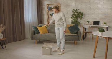 Bir kadın şişe temizleyicisinden, şık bir oturma odasında, rahat bir kanepesi olan bir kovaya döker..