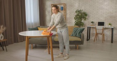 Bir kadın şık bir oturma odasında, modern ve rahat bir ortamda renkli giysileri bir masanın üzerine katlıyor..