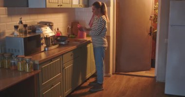 Gündelik giysiler içinde genç bir kadın akşamları parlak ve modern bir mutfakta ıslak ellerini kağıt havlularla kurutuyor. Günlük rutin, yaşam tarzı.