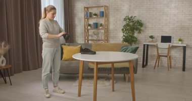 Bir kadın şık bir odada duruyor, siyah bir ayakkabıyı beyaz bir masada fırçalıyor. Oda modern mobilyalarla döşenmiş ve ışıkla dolu..