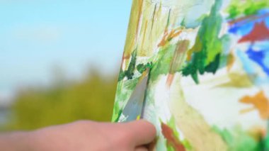 Renkli bir manzara resminin kapanışı palet bıçağıyla yapılmış, zengin dokular sergileniyor..