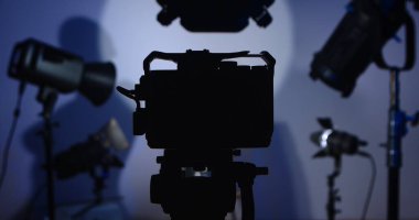 Fotoğraf stüdyosundaki bir kameranın silueti ve ışıklandırma ekipmanları. Profesyonel ışıklandırma ekipmanıyla sahne arkası fotoğraf çekimi.