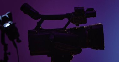 Profesyonel video kameranın siluetini mor bir arkaplana yaklaştır. Sahne arkası fotoğraf çekimi.