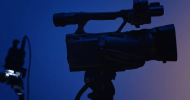 Profesyonel video kameranın siluetini mavi bir arkaplana yaklaştır. Sahne arkası fotoğraf çekimi.