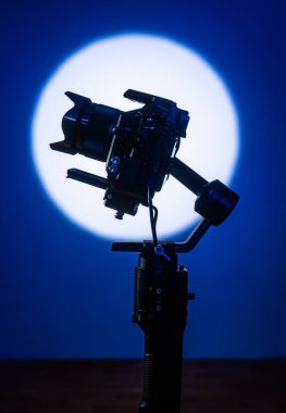 Motosikletli bir dengeleyiciye monte edilmiş profesyonel bir kameranın yan görüntüsü, derin mavi arka planda parlak bir dairesel ışığa karşı çekilmiş, film yapımcılığını sembolize ediyor..