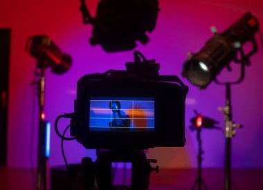 Kameranın yakın çekim görüntüsü bir manken ve mavi ve pembe tonlarında dramatik ışıklandırmalı renkli bir stüdyo görüntüsü yakalıyor. Profesyonel ışıklandırma ekipmanıyla sahne arkası fotoğraf çekimi.