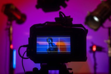 Kameranın yakın çekim görüntüsü bir manken ve mavi ve pembe tonlarında dramatik ışıklandırmalı renkli bir stüdyo görüntüsü yakalıyor. Profesyonel ışıklandırma ekipmanıyla sahne arkası fotoğraf çekimi.