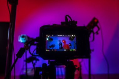 Kameranın yakın çekim görüntüsü bir manken ve mavi ve pembe tonlarında dramatik ışıklandırmalı renkli bir stüdyo görüntüsü yakalıyor. Profesyonel ışıklandırma ekipmanıyla sahne arkası fotoğraf çekimi.