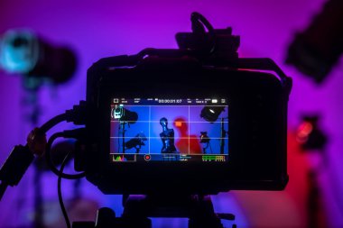 Kameranın yakın çekim görüntüsü bir manken ve mavi ve pembe tonlarında dramatik ışıklandırmalı renkli bir stüdyo görüntüsü yakalıyor. Profesyonel ışıklandırma ekipmanıyla sahne arkası fotoğraf çekimi.