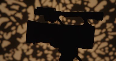 Profesyonel bir kameranın silueti, yaratıcılığı vurgulayan, sanatsal bir arka plana karşı..