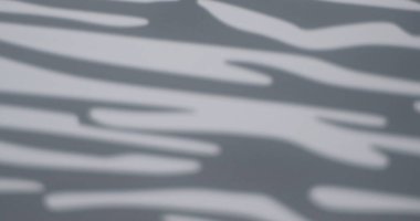 Soyut gölge deseni, gri bir yüzeyde doğal ışık yansımalarını andıran dalgalı çizgiler oluşturuyor..