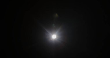 Parlak bir ışık parlaması, karanlık bir arkaplanda parıltı yaratarak gizem hissi uyandırıyor. Siyah arka planda gerçek optik mercek parlıyor, yıldız parlıyor.