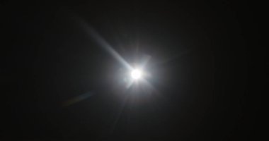 Parlak bir ışık parlaması, karanlık bir arkaplanda parıltı yaratarak gizem hissi uyandırıyor. Siyah arka planda gerçek optik mercek parlıyor, yıldız parlıyor.