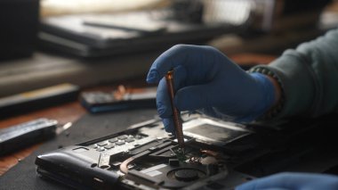Bir dizüstü bilgisayarın iç kısımlarını onarmak için tornavida kullanan mavi eldiven takan birini kapat..