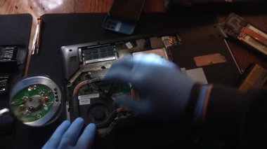 Parçalanmış bir dizüstü bilgisayarın iç parçaları üzerinde çalışan eldiven giyen bir teknisyenin yakından görüntüsü büyüteç altında bileşenleri gösteriyor. Yavaş çekim.