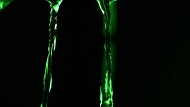 Parlayan yeşil su akıntılarının soyut yakın plan derinliği siyah arkaplan üzerine düşen, dramatik neon ışıkla aydınlatılan ve metin veya tasarım için merkezde boş kopya alanı bırakan.