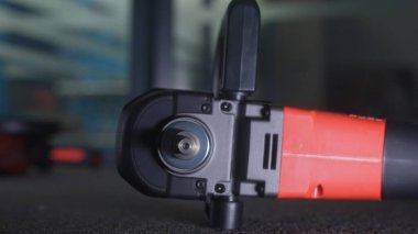 Koyu renk bir yüzeye yerleştirilmiş kırmızı ve siyah bir elektrik açı öğütücüsünün ayrıntılı görüntüsü, araçların mekanizmasını gösteriyor.