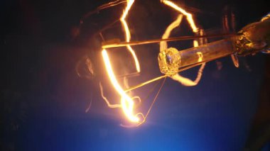 Koyu bir ortamda parlayan bir ampul filamanının detaylı görüntüsü, sıcak ve canlı renkler yakalıyor..