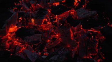 Koyu bir ızgarada parlayan kömür közlerine, turuncu ısıya ve uçan kıvılcımlara yakın durun. Barbekü, yakıt, enerji ve yüksek sıcaklık kavramları için dramatik yangın arka planı.