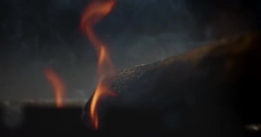 Düşük tuşlu turuncu alevler ve karanlık bir kütüğün arkasında duman, ısı, tehlike, barbekü ve atmosferik kavramlar için karamsar bir yangın arka planı oluşturur..