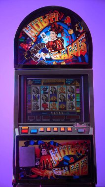 Dnipro, Ukrayna - 17 Şubat 2026: Renkli bir Multi Game joker tasarımı ve ekranda Aztek Gold oyunu olan eski kumarhane slot makinesi, canlı mor gradyan arkaplana karşı duruyor.