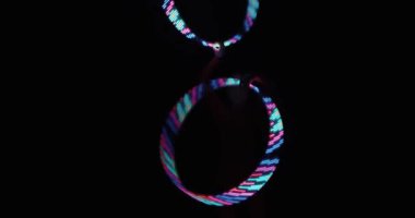 Sirkte çalışan bir kadın sanatçı, LED halkaları karanlıkta döndürerek stüdyonun siyah arka planına karşı ışık yollarından parlak neon şekiller yaratıyor. Yavaş çekim.
